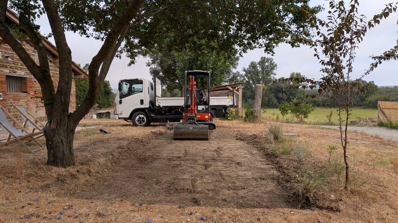 Terrain nivelé et remis en état en fin de chantier, minipelle et camion benne au second plan